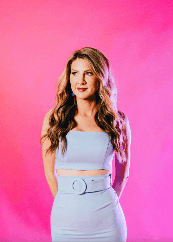 Woman with long wavy hair in pastel outfit against pink background.