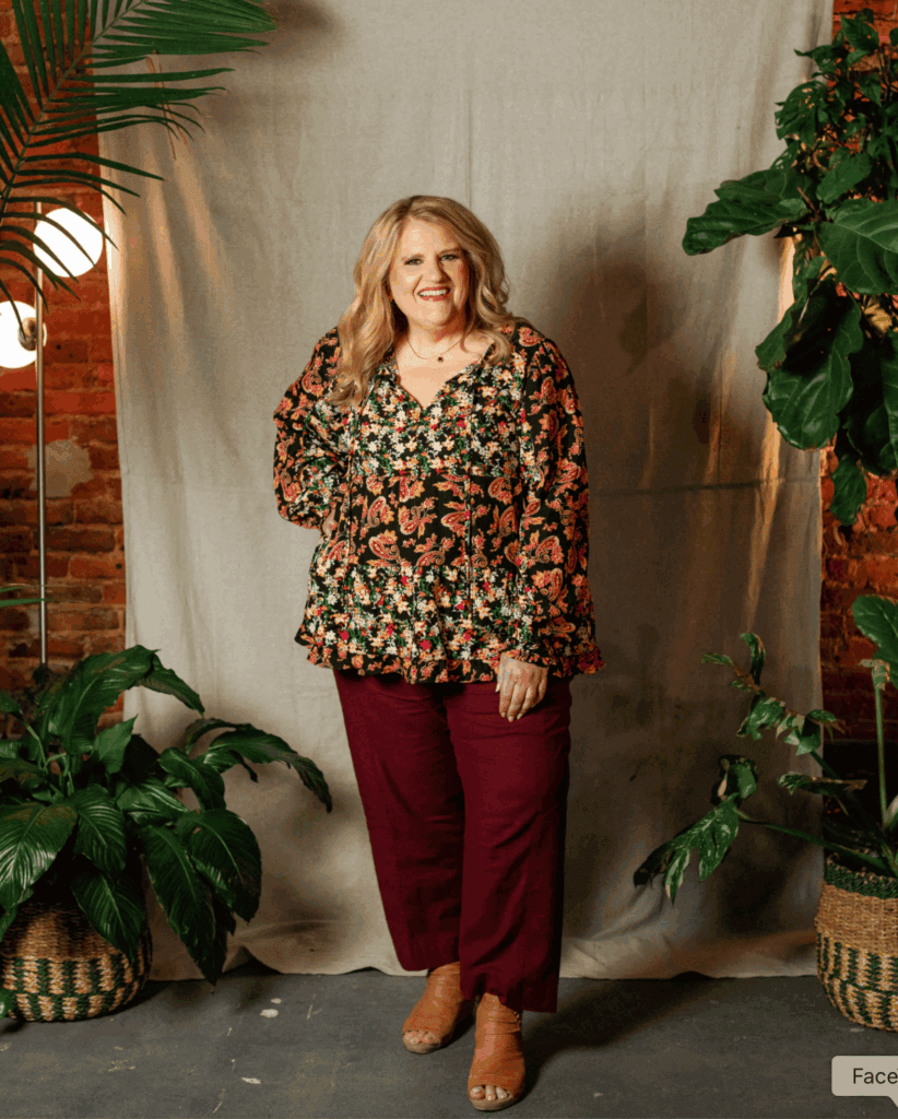 Woman smiling in floral blouse and burgundy pants at Upper Cumberland Lifestyle event.