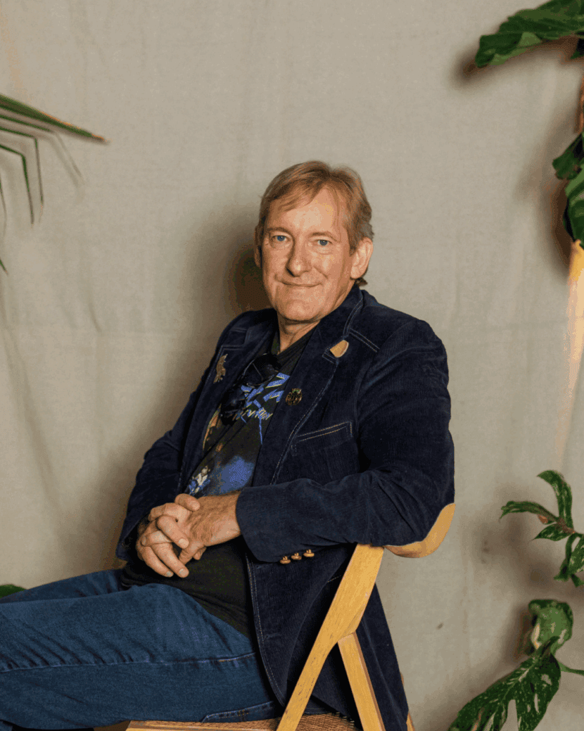 Elderly man sitting comfortably in a cozy indoor setting with plants.