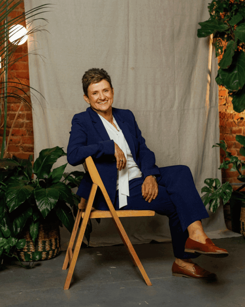Portrait of a smiling woman in a blue suit sitting on a wooden chair.