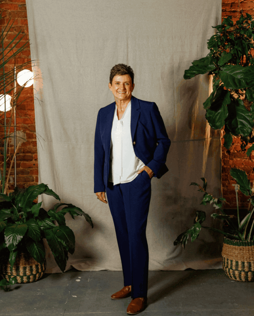 Woman in business suit standing with plants in a studio setting.