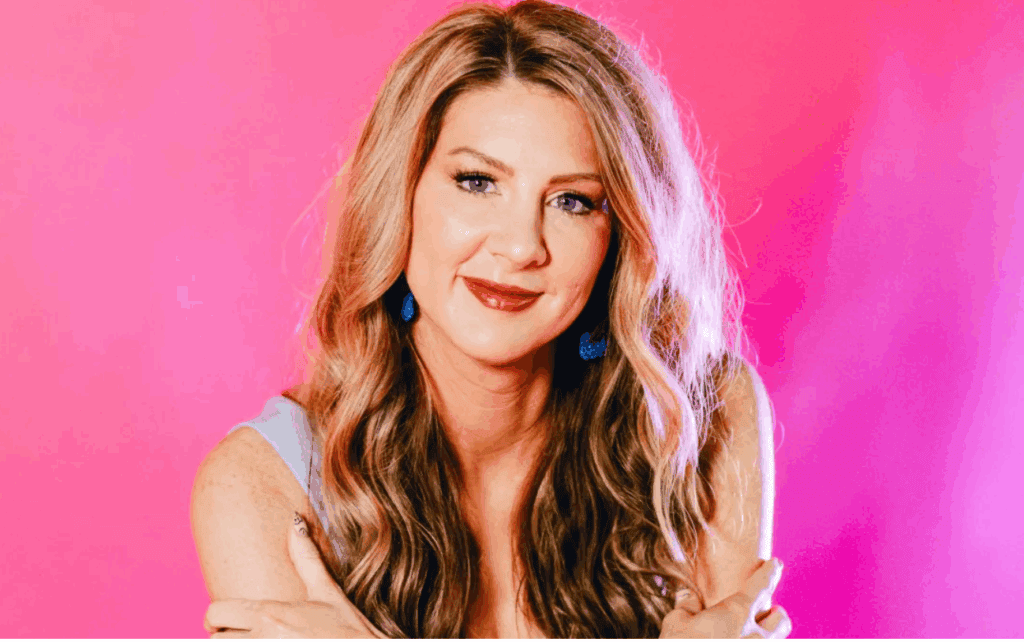 Woman with long wavy hair smiling against pink background.