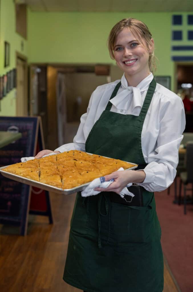 Delicious homemade dessert presented by a cheerful waitress in a cozy restaurant setting.