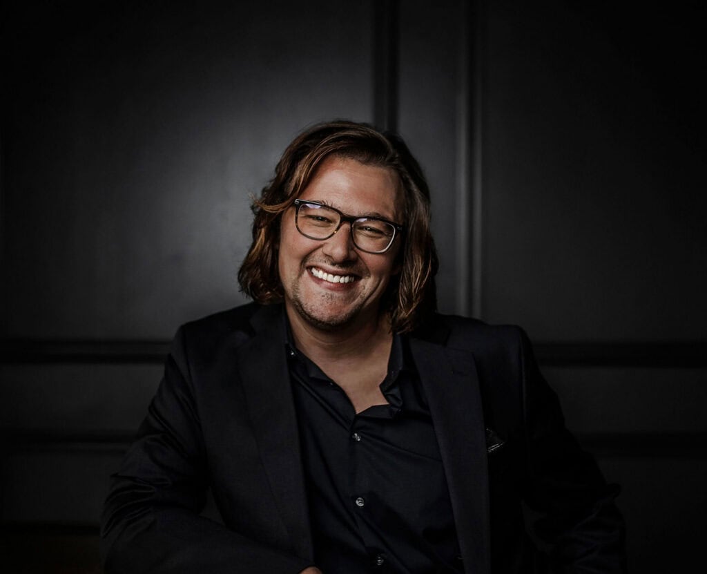 Smiling man with glasses in a black suit, professional portrait.