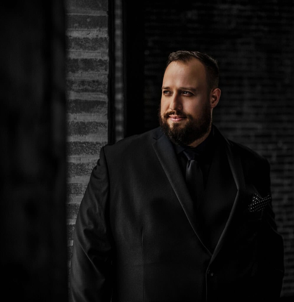 man looks off in all black on black wall