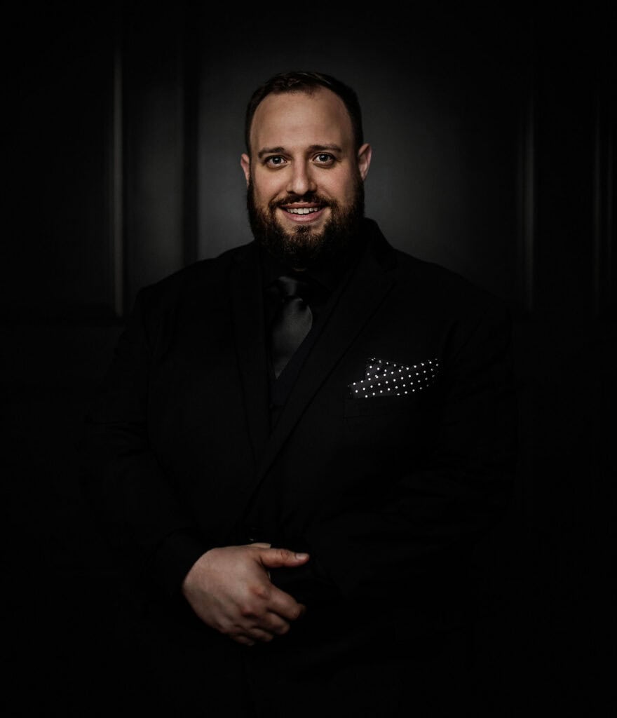 man smiles in all black on black wall