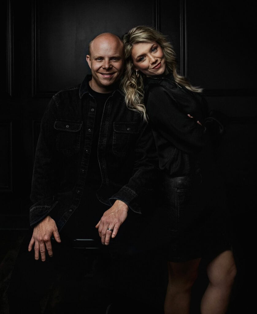 couple smiles lovingly in all black outfits on black wall