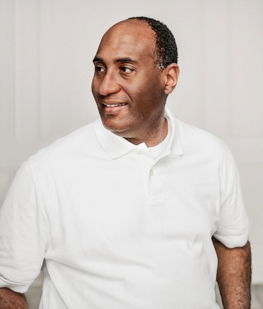 black man in all white smiling on white wall