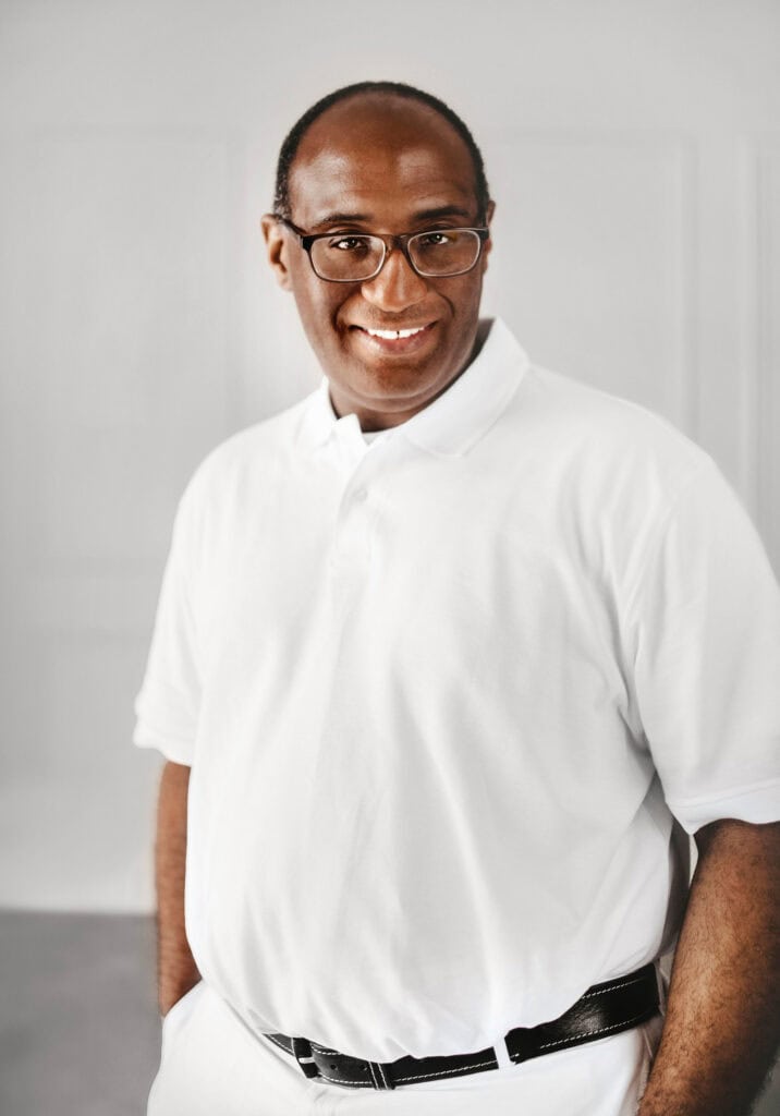 black man in all white smiling on white wall
