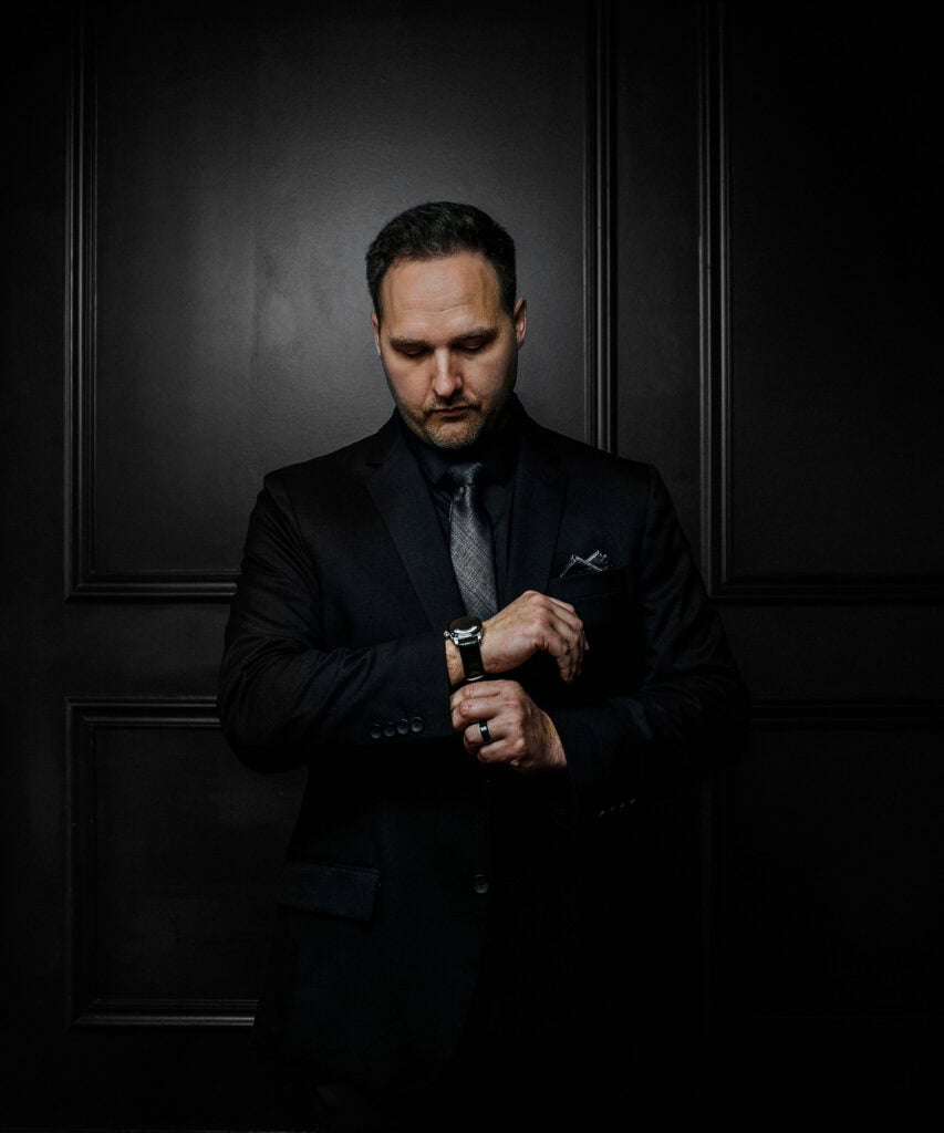 man in all black looks at watch on black wall