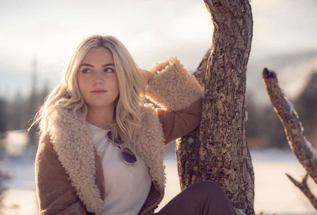 Young woman sitting by a tree in a winter landscape, enjoying the outdoors.