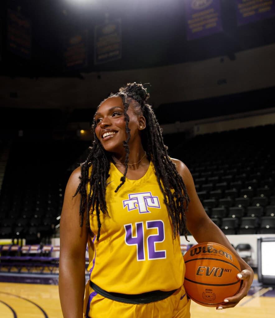 Female basketball player in yellow jersey holding a basketball on court.